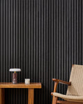 Black NORDAN acoustic slat wood wall panels installed as a feature wall in a reading corner.